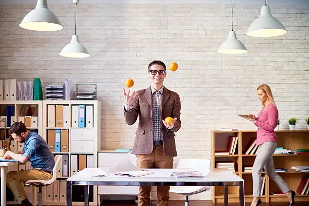 Joyful designer juggling with oranges at design studio