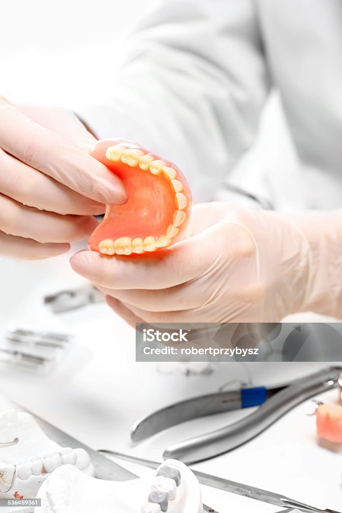 Dentures, partial dentures. Prosthetics hands while working on the denture, false teeth, a study and a table with dental tools. Cosmetic Dentistry Stock Photo