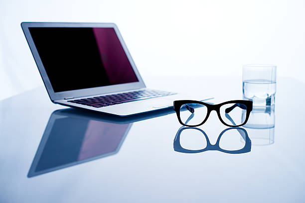 Eyeglasses, laptop and glass of water on glossy table