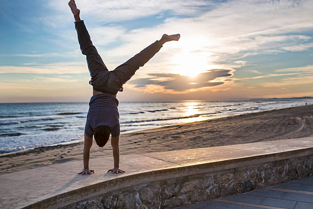 One young men practising handstand hold street workout in the beachat sunset.