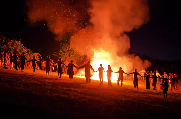 People holding hands and dancing in a circle around a fire at night