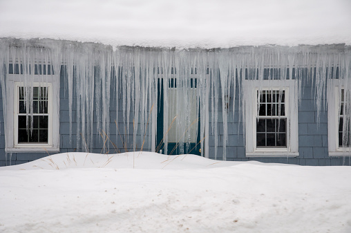 Small blue house facade with door and windows covered by long icicles, in Massachusetts.