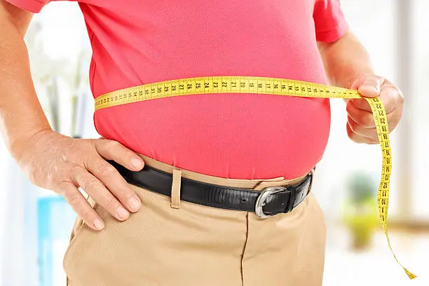 Close-up on a man measuring his belly at home
