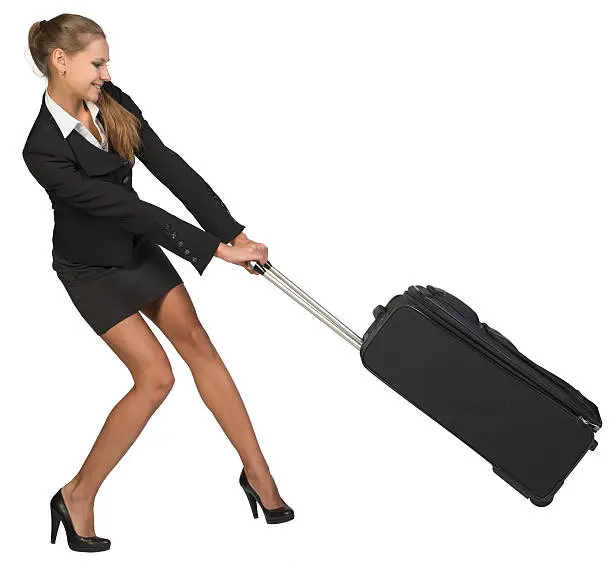 Photo of Businesswoman dragging heavy wheeled suitcase at utmost strain