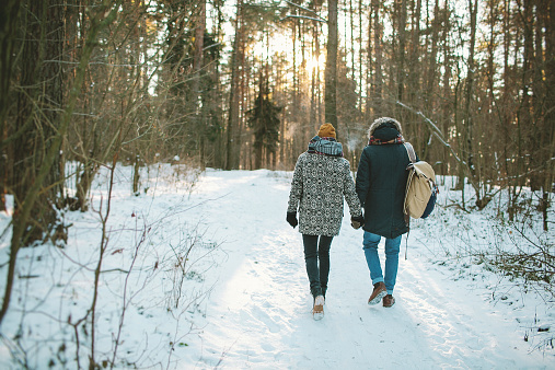 Young hipster couple having a walk in winter forest with bag alone