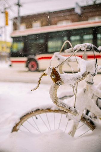 Bicycles buried in heavy snow on the sidewalk on urban street of the city during the winter storm.
