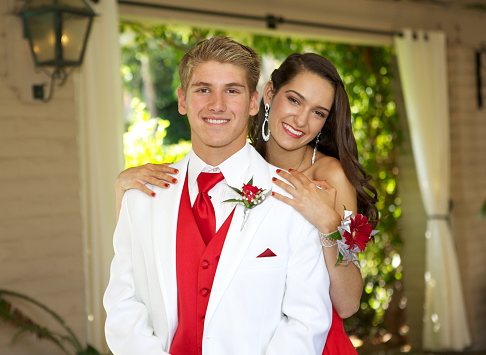 An attractive couple posing for a prom photo.  The boy is in the front with his white tuxedo.