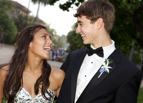 A young couple going to the prom are laughing and looking at each other.