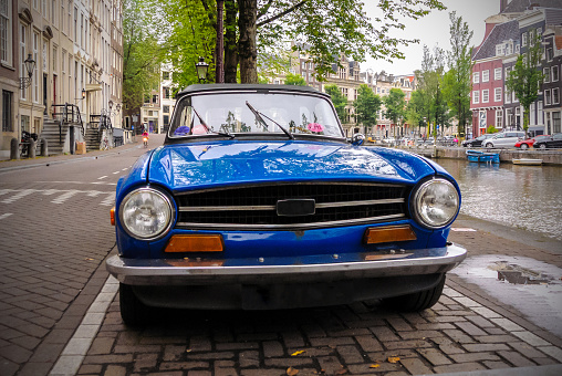 Vintage blue car is parked on the street along a canal in Amsterdam, Netherlands