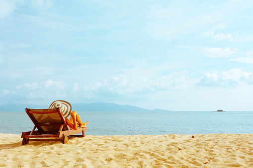 Asian man in casual clothing resting on beach chair at tropical beach. Happy guy sunbathing or nap on sunbed by the sea in sunny day.  Young man relax and enjoy outdoor activity lifestyle on summer holiday vacation