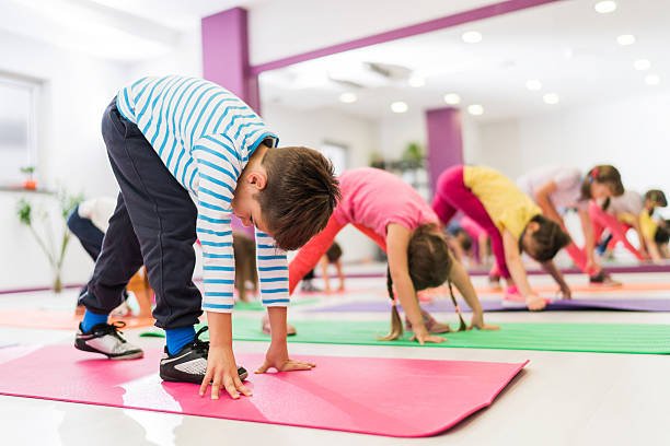 Group of kids stretching their legs on a sports training. Large group of children doing stretching exercises in a health club. Focus is on boy in striped t-shirt. gymnastics stock pictures, royalty-free photos & images