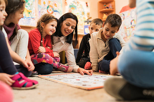Happy preschool teacher educating large group of children in kindergarten. Happy female teacher teaching group of small kids in a preschool. child care photos stock pictures, royalty-free photos & images