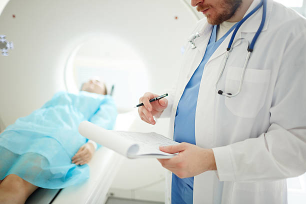 Doctor at CT scan machine Doctor checking medical record of his patient during CT scan tomography stock pictures, royalty-free photos & images