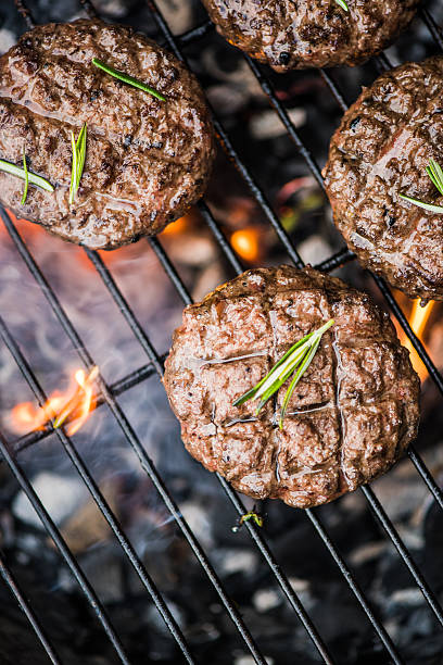 beef burgers on grill with flames stock photo