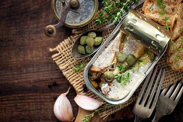 Canned sardines with capers Open tin of sardines in olive oil with capers and thyme on dark rustic wooden background preserved food stock pictures, royalty-free photos & images