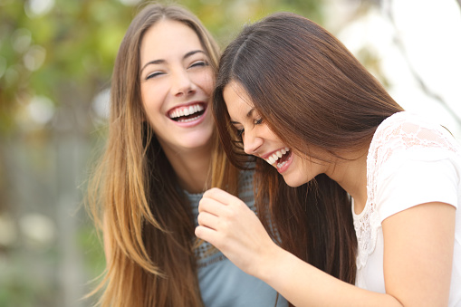 Two happy woman friends laughing together in a park with a green background