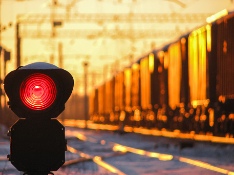 Railway traffic light at sunset shows red signal on railway. Red light. Moving train on the background.