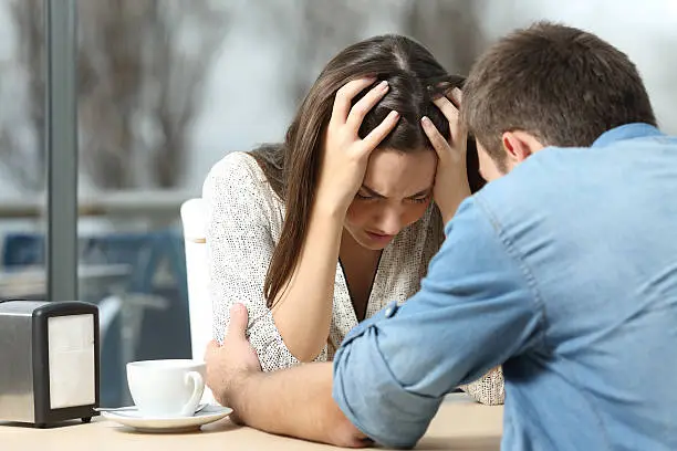 Male comforting to a sad depressed female who needs help in a coffee shop. Break up or best friend concept