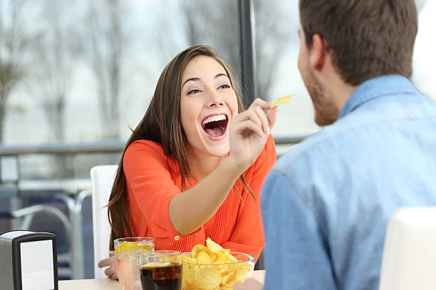 Playful couple eating chip potatoes Playful couple eating chip potatoes and joking looking each other in a date in a coffee shop family eating potato chips stock pictures, royalty-free photos & images
