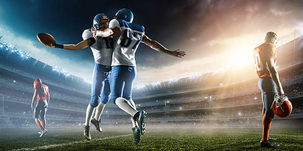 Two Football Players celebrate their victory Two Football Players celebrate their victory. The action takes place on professional stadium. The opposite team players are sad. Players wear unbranded sports uniform. There is artificial light on stadium together with sunlight. american football sport photos stock pictures, royalty-free photos & images