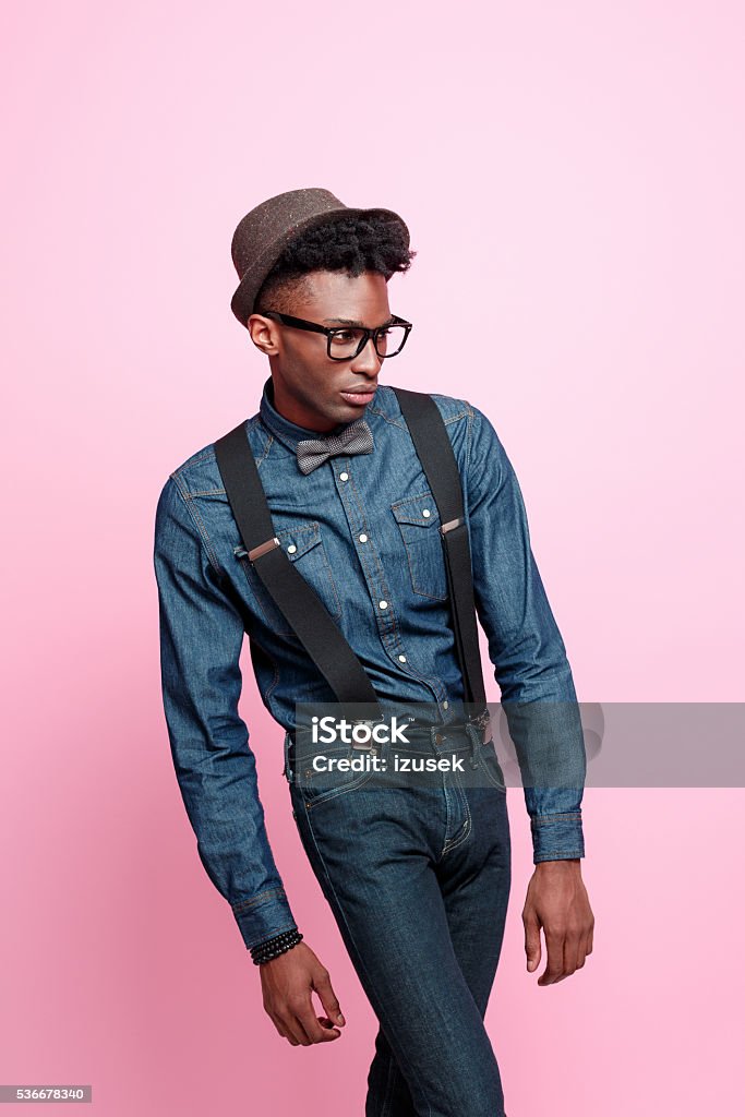 Portrait of fashionable afro american young man Studio portrait of fashionable afro american young man wearing denim shirt and trausers, hat, nerd glasses and bow tie. Studio portrait, pink background. Small Business Stock Photo