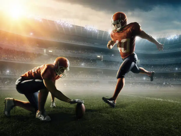 Professional American football players perform kick off on a professional sport stadium with spotlight. Players  wear unbranded football cloths. 