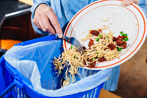 Woman scraping food leftovers into bin Close-up of a woman sweeping the leftovers from a meal into a blue garbage bin. AdobeRGB colorspace. excess stock pictures, royalty-free photos & images