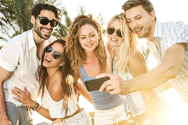 Group of happy people taking a selfie with smart phone at sunset.