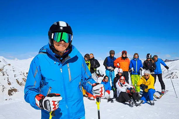 Happy smiling men snow skier skiing, twelve friends, behind him a group of friends enjoying on sunny ski resorts. Resting, sunbathe against blue sky.  Developed from RAW,  Adobe RGB color profile. Shallow DOF  for soft background.