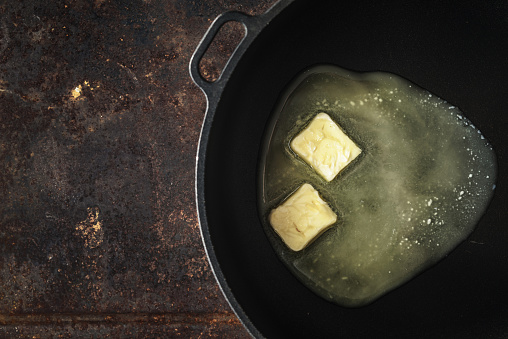 Pieces of butter in the hot pan  on the metal background top view