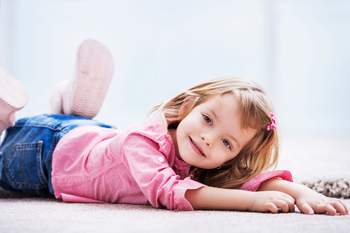 Smiling little girl lying on carpet and looking at the camera.  