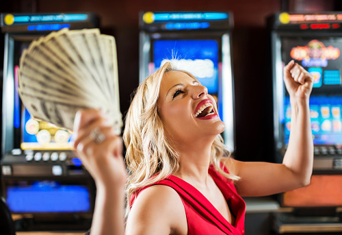 Happy mid adult woman winning money on a slot machine in a casino and celebrating.