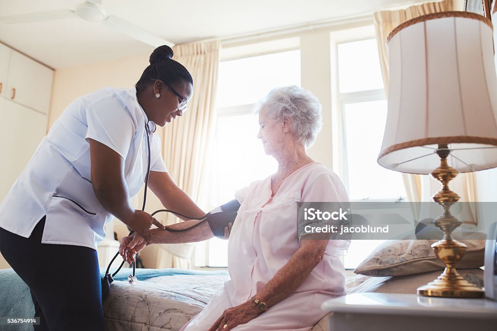 Nurse checking blood pressure of female patient Female nurse doing blood pressure measurement of a senior woman patient. Doctor checking blood pressure of an elderly woman at old age home. Nurse Stock Photo