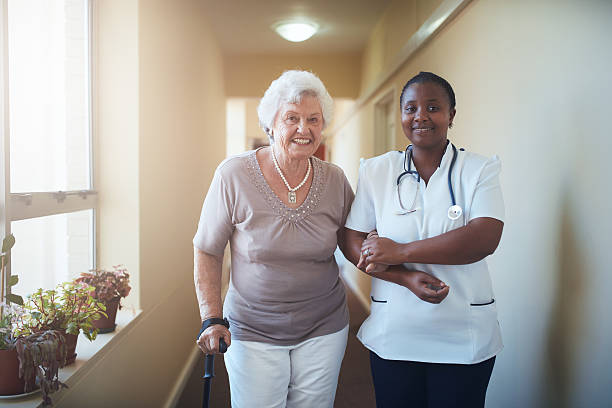 Nurse assisting a senior patient to walk Caring female nurse assisting a senior patient to walk. Healthcare worker and senior woman together at nursing home orthopedics photos stock pictures, royalty-free photos & images