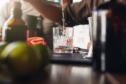 Closeup shot of bartender pouring drink into a glass on counter. Barman preparing cocktail.