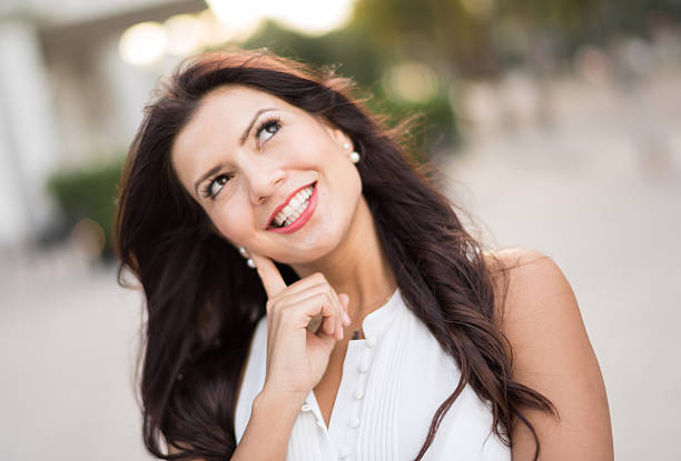 Woman portrait thinking and looking up while smiling on the street
