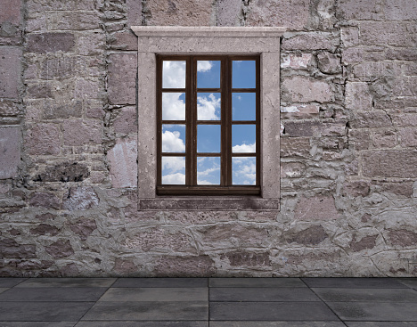Old window against a stone wall with a view of sky and clouds.