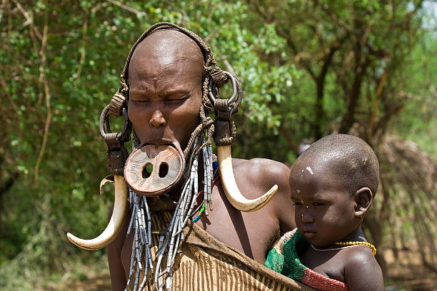 Woman with her baby of the Mursi tribe. Omo Valley, Ethiopia - March 13, 2010: Woman of the Mursi tribe with traditional ornaments and lip plate carries her baby in her village in the Omo valley, Ethiopia. omo river photos stock pictures, royalty-free photos & images