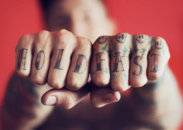 Displaying his motto for the world to see Closeup shot of man showing the tattoos on his fingers against a red backgroundhttp://195.154.178.81/DATA/istock_collage/356320/shoots/780556.jpg arm tattoo ideas for men pictures stock pictures, royalty-free photos & images