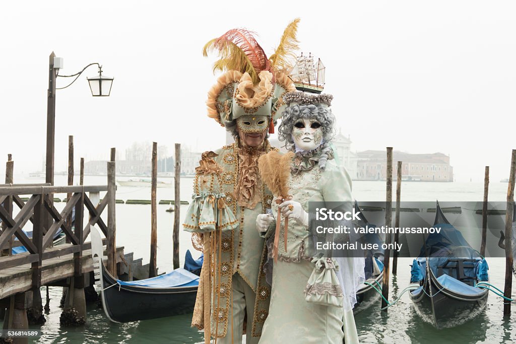 Venetian Couple Venice, Italy- February 8, 2015. A couple disguised in Venetian costumes pose in front of gondolas dock during the Venice Carnival days. Period Costume Stock Photo