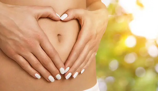 Body care, pregnancy or diet concept, female hands forming heart shape on the stomach
