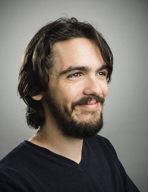 Studio portrait of a caucasian young man with happy expression. The man has around 30 years and has long hair and glasses. Vertical color image from a DSLR camera. Sharp focus on eyes.