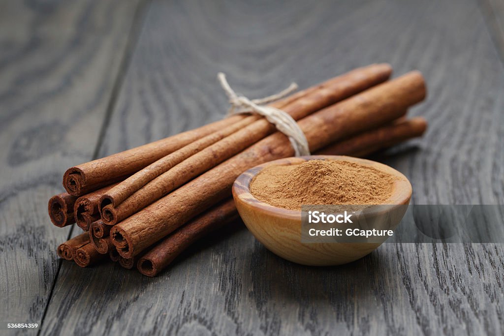 bunch of cinnamon sticks tied with twine and powder bunch of cinnamon sticks tied with twine and powder in bowl, on rustic oak table 2015 Stock Photo