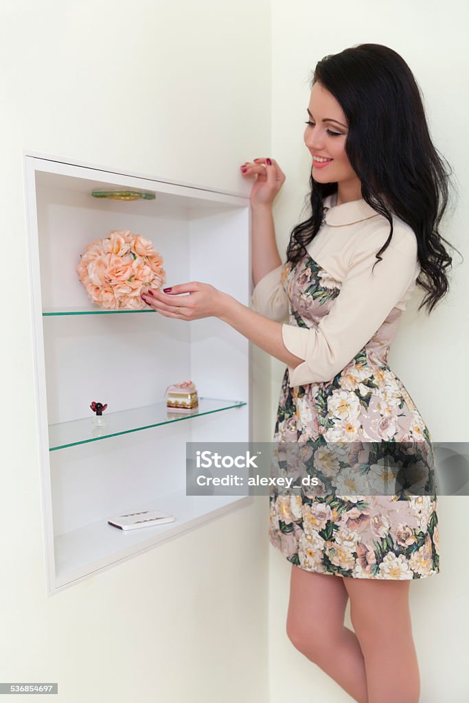 Young brunette woman puts fragile artificial flowers on shelf 2015 Stock Photo