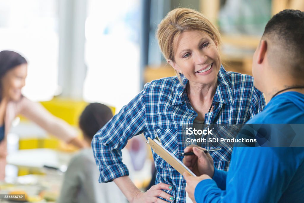 Mature woman talking with volunteer in community soup kitchen Teaching Stock Photo