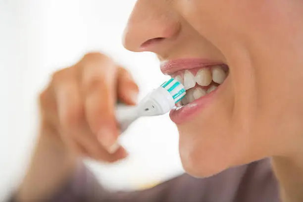 Closeup on young woman brushing teeth.