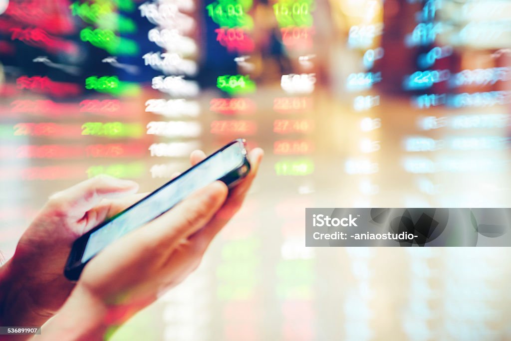cell phone on hand with stock market data background Concepts Stock Photo
