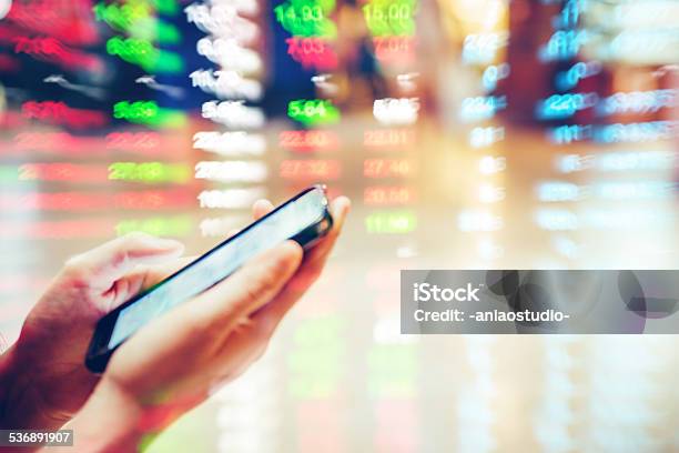 Cell Phone On Hand With Stock Market Data Background Stock Photo - Download Image Now