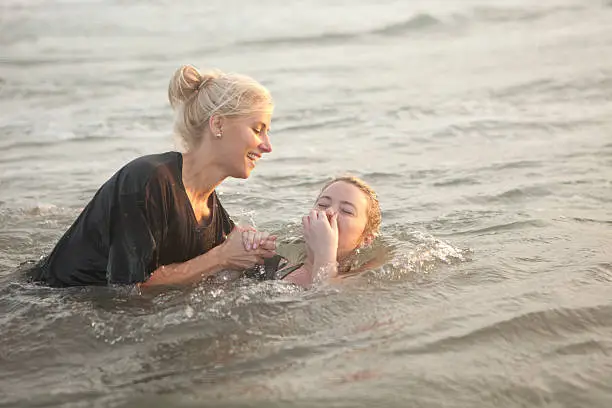 A woman baptizes a young woman in the ocean during sunsetA woman baptizes a young woman in the ocean during sunset