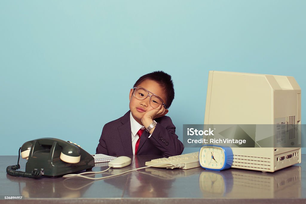 Young Japanese Boy Tired at the Office A young Japanese boy dressed as a businessman and executive sits at his desk and is bored from the lack of work. Boy is ready to do good business. Retro styled. Boredom Stock Photo